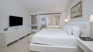 A modern bedroom with a large bed, a flat-screen TV, a bedside table, and a door leading to another room. - Ski-in/ski-out condominium at the base of Vail Mountain. Best location, pool!! (Vail)