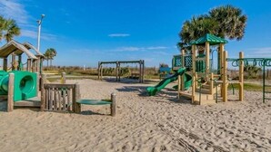 Une aire de jeux de plage avec un toboggan, des balançoires et un petit abri.