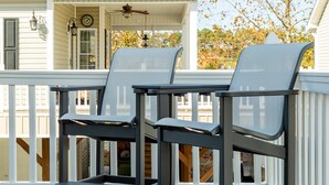 Une terrasse avec deux chaises et une table, une maison avec un porche, et des arbres aux couleurs automnales en arrière-plan.