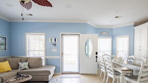 Un salon avec un canapé d’angle, une table à manger avec des chaises blanches et un ventilateur de plafond.