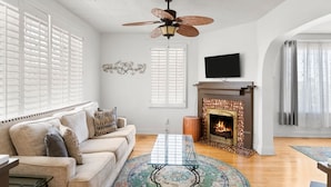 A living room with a beige sofa, a glass coffee table, a fireplace, and a ceiling fan. - 3 story home near downtown El Paso  (El Paso)