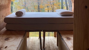 Una cabana de fusta amb un llit i una finestra circular gran que fa vedar a un bosc.