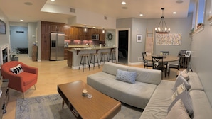 A modern living room with a sofa, armchair, and coffee table. A kitchen with wooden cabinets and stainless steel appliances is visible in the background. - Historic Condo in the Heart of Mount Adams (Cincinnati)