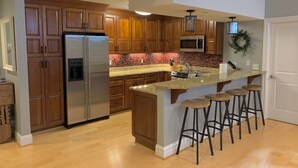 A modern kitchen with wooden cabinets, stainless steel appliances, a granite countertop, and bar stools. - Historic Condo in the Heart of Mount Adams (Cincinnati)
