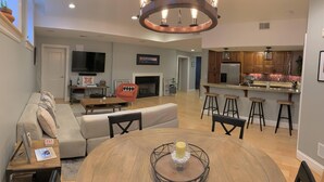 A modern living room with a sofa, coffee table, and a dining table with chairs. There is a kitchen area with a refrigerator, stove, and bar stools. - Historic Condo in the Heart of Mount Adams (Cincinnati)