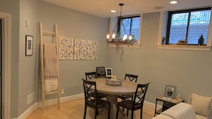 A dining area with a round table, four chairs, a chandelier, and a window with a view of the outside. - Historic Condo in the Heart of Mount Adams (Cincinnati)