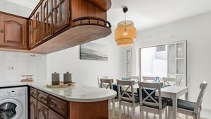 A kitchen with wooden cabinets, a built-in washing machine, a marble countertop, and a dining area with white chairs and a table. - Sea La Vie Quintessential Algarve Villa with Pool in Manta Rota (Vila Nova de Cacela)