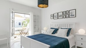 A bedroom with a white bed, a white nightstand, a white dresser, and a large window with a view of the outside. - Sea La Vie Quintessential Algarve Villa with Pool in Manta Rota (Vila Nova de Cacela)