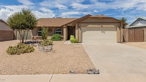 A residential house with a garage, a driveway, and a landscaped front yard with cacti and rocks. - Desert Escape with Private Heated Pool & Backyard (Peoria)