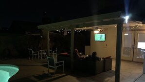 An outdoor patio area with a pool, seating, and a TV screen. - Desert Escape with Private Heated Pool & Backyard (Peoria)