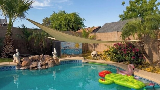 A swimming pool with a rock feature, a mural, and a shaded area. - Desert Escape with Private Heated Pool & Backyard (Peoria)