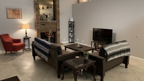 A living room with a fireplace, a TV, a red armchair, a sofa, and a coffee table. - Desert Escape with Private Heated Pool & Backyard (Peoria)
