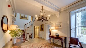 Un vaste hall d’entrée orné d’un lustre, avec un escalier, une grande fenêtre et un tapis à motifs.