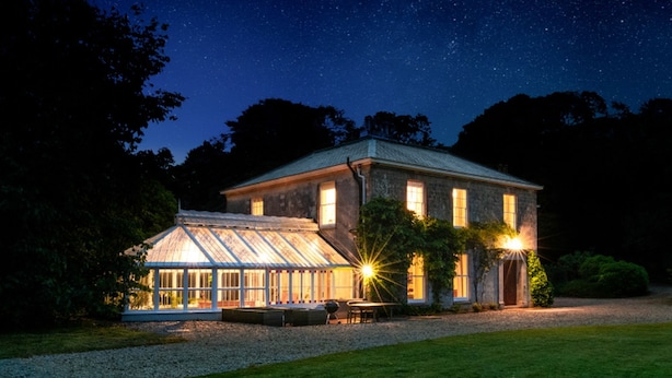 Une grande maison à deux étages, dotée d’une véranda en verre et d’une pelouse bien entretenue.