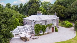 Une grande maison en pierre dotée d’une véranda, entourée d’une végétation luxuriante.