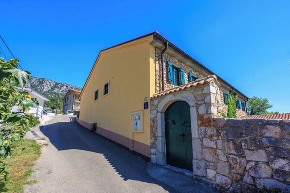 A narrow street with a yellow building featuring a stone entrance and blue shutters.