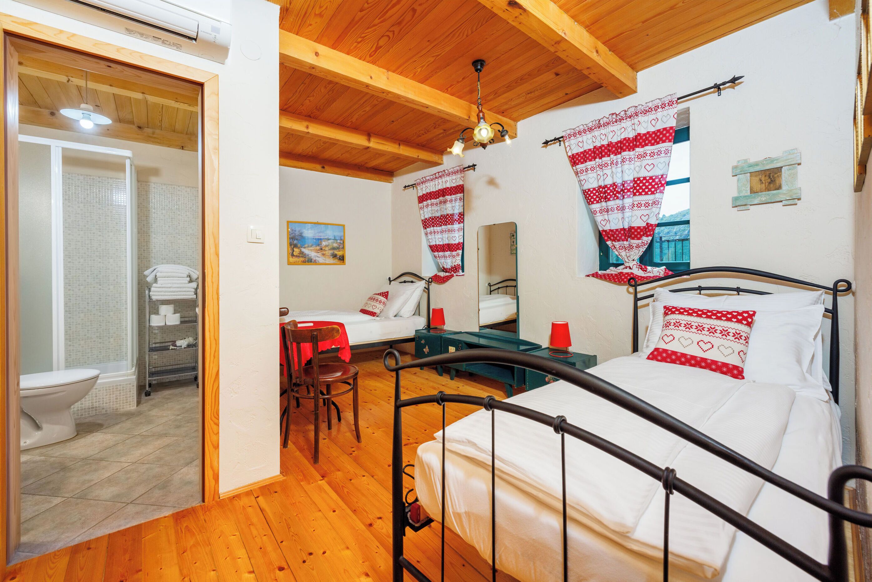 A bedroom with a wooden ceiling, a metal bed frame, a white mattress, and red heart-patterned curtains.