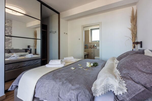 Une chambre moderne avec un grand lit, une table de chevet, un miroir et une vue sur la salle de bain.