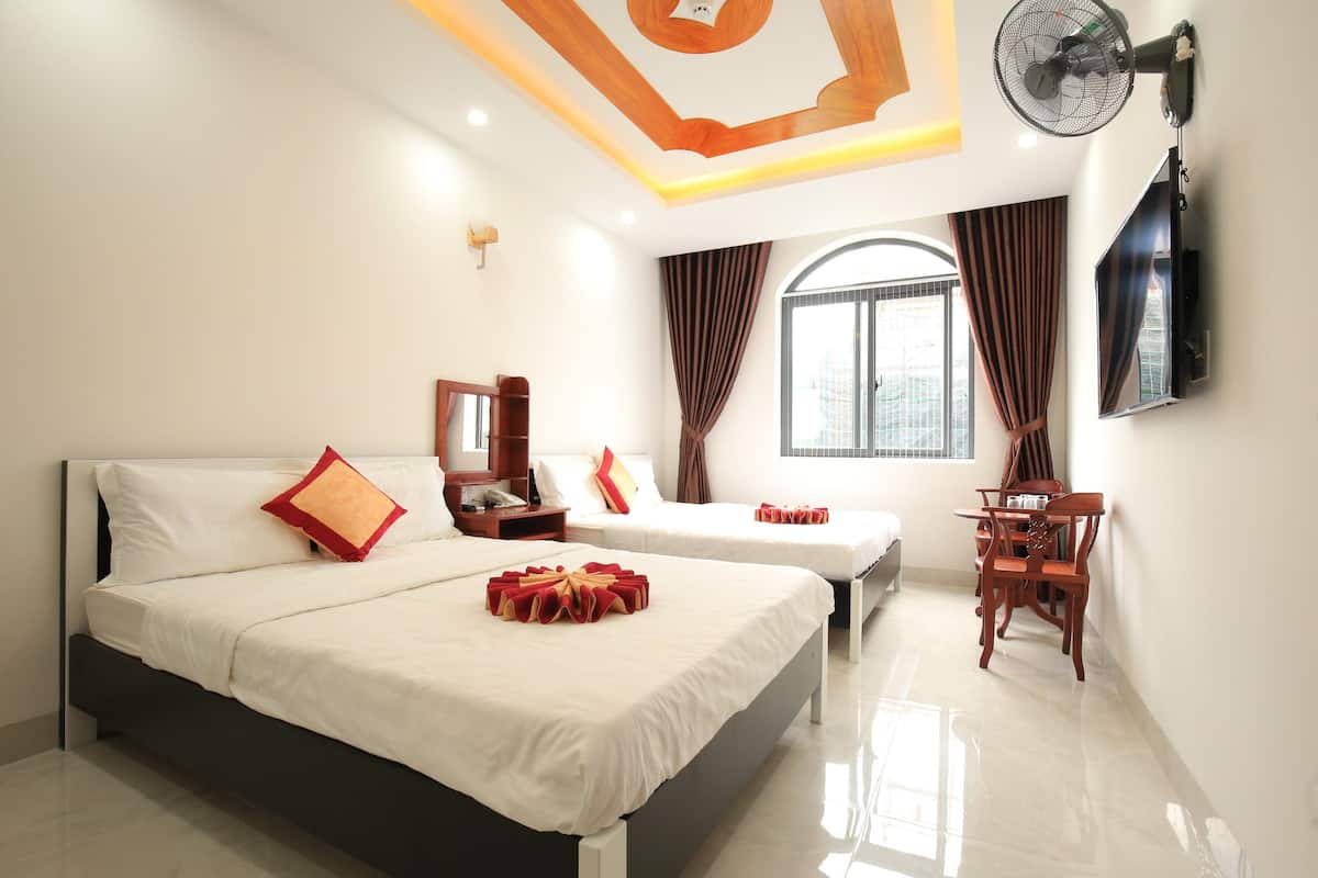 A hotel room with two beds, a desk, a chair, a TV, and a window with curtains.