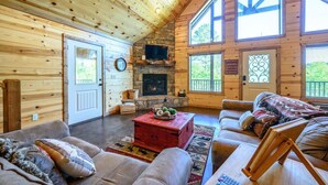A cozy cabin interior with a stone fireplace, wooden walls, and large windows.