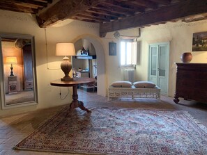 A room with a patterned rug, a round table with a lamp, a bench with cushions, and a wooden dresser. - Panorama Toscano with Splendid Sea Views, Terrace and Whirlpool (Metato)