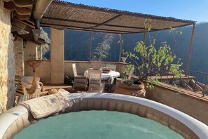 Un área de jacuzzi con sillones de mimbre y una mesa, rodeada de plantas en macetas y con vistas panorámicas.