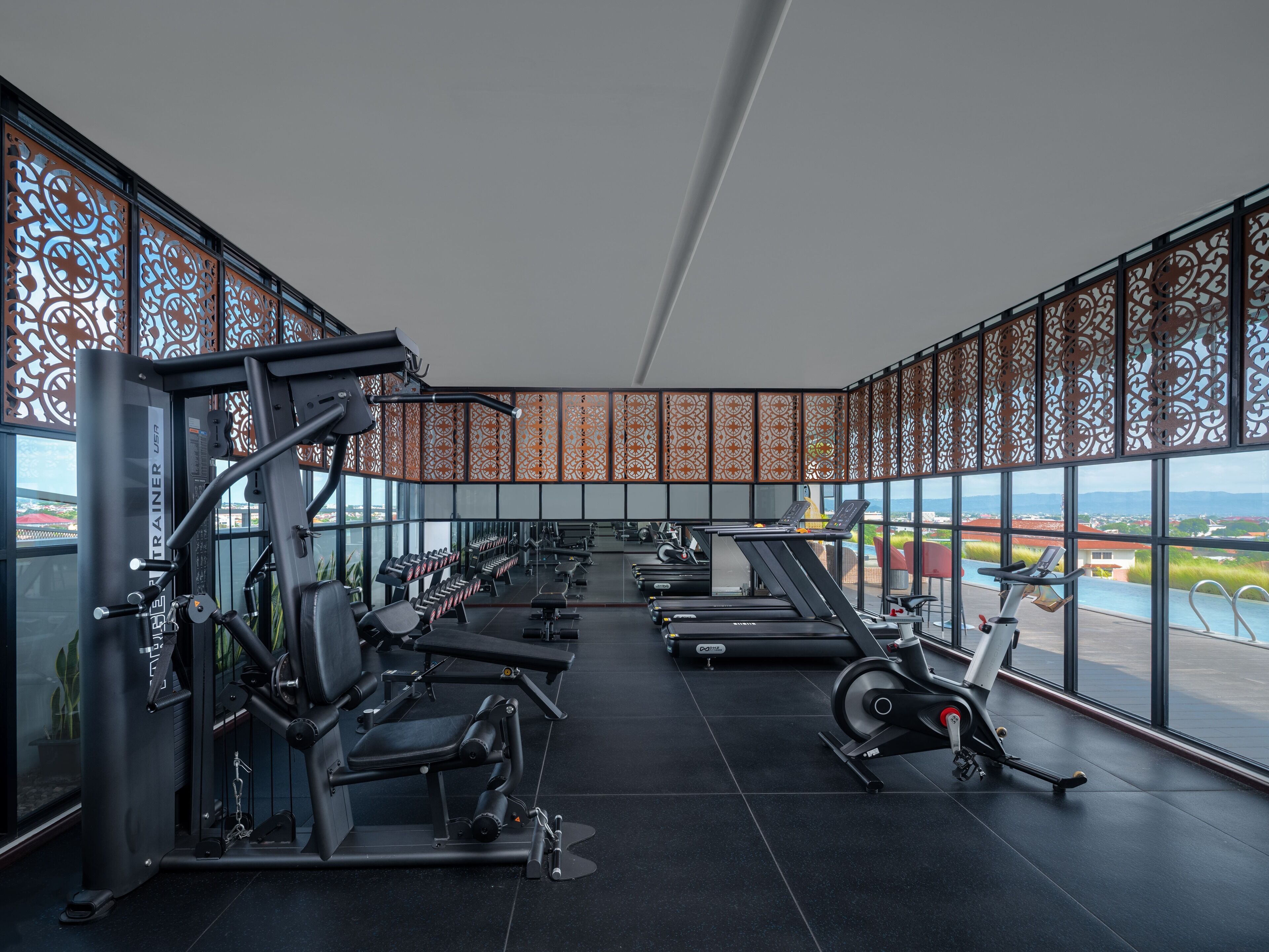 A modern gym with various exercise equipment, large windows, and a view of a cityscape.