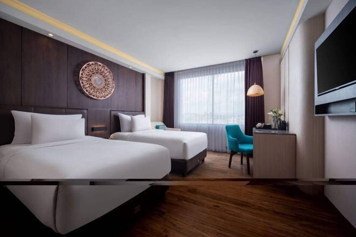 A hotel room with two beds, a TV, a desk, a chair, and a decorative wall piece.