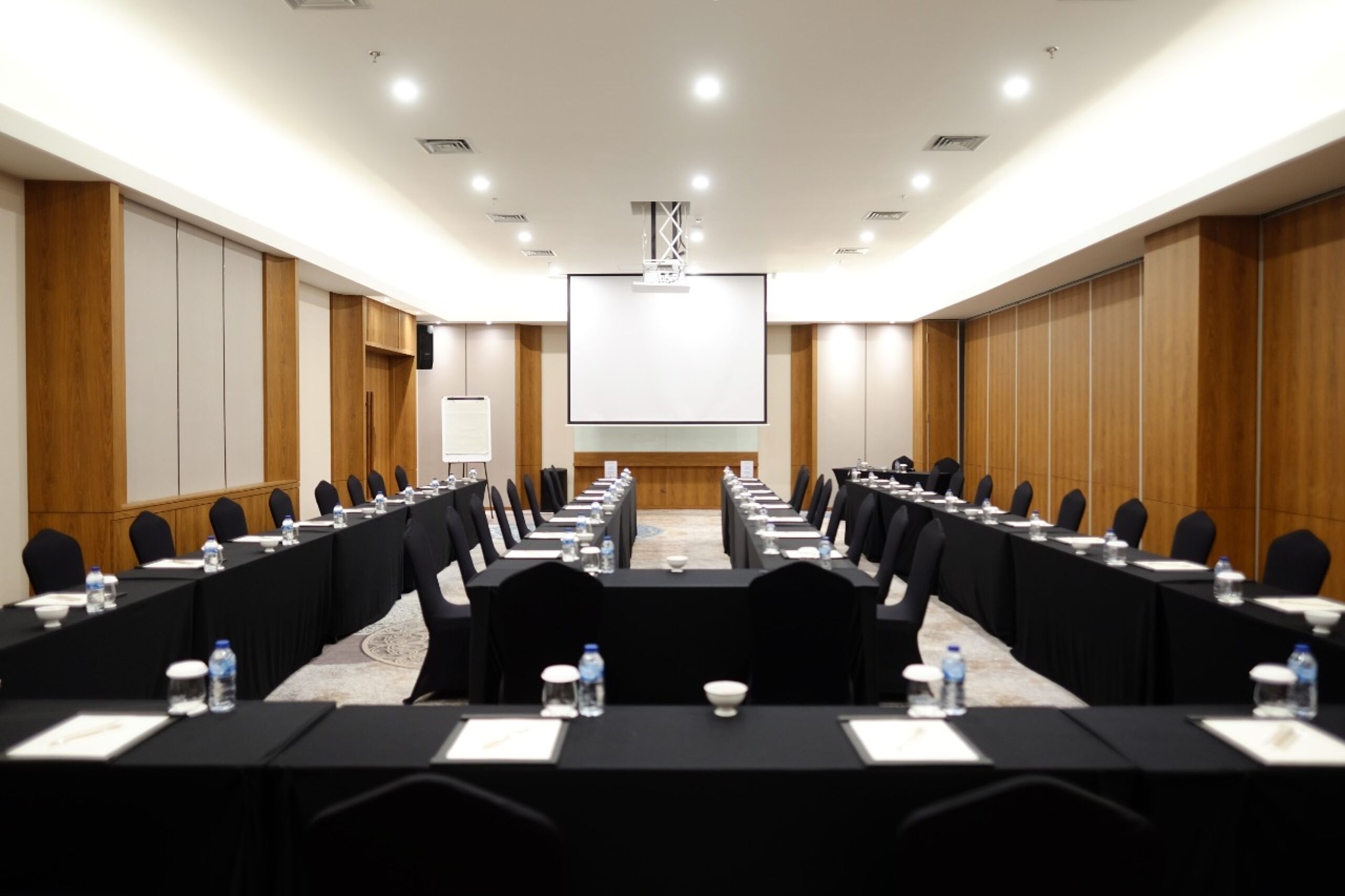 A conference room with a long table, chairs, and a projector screen at the front.
