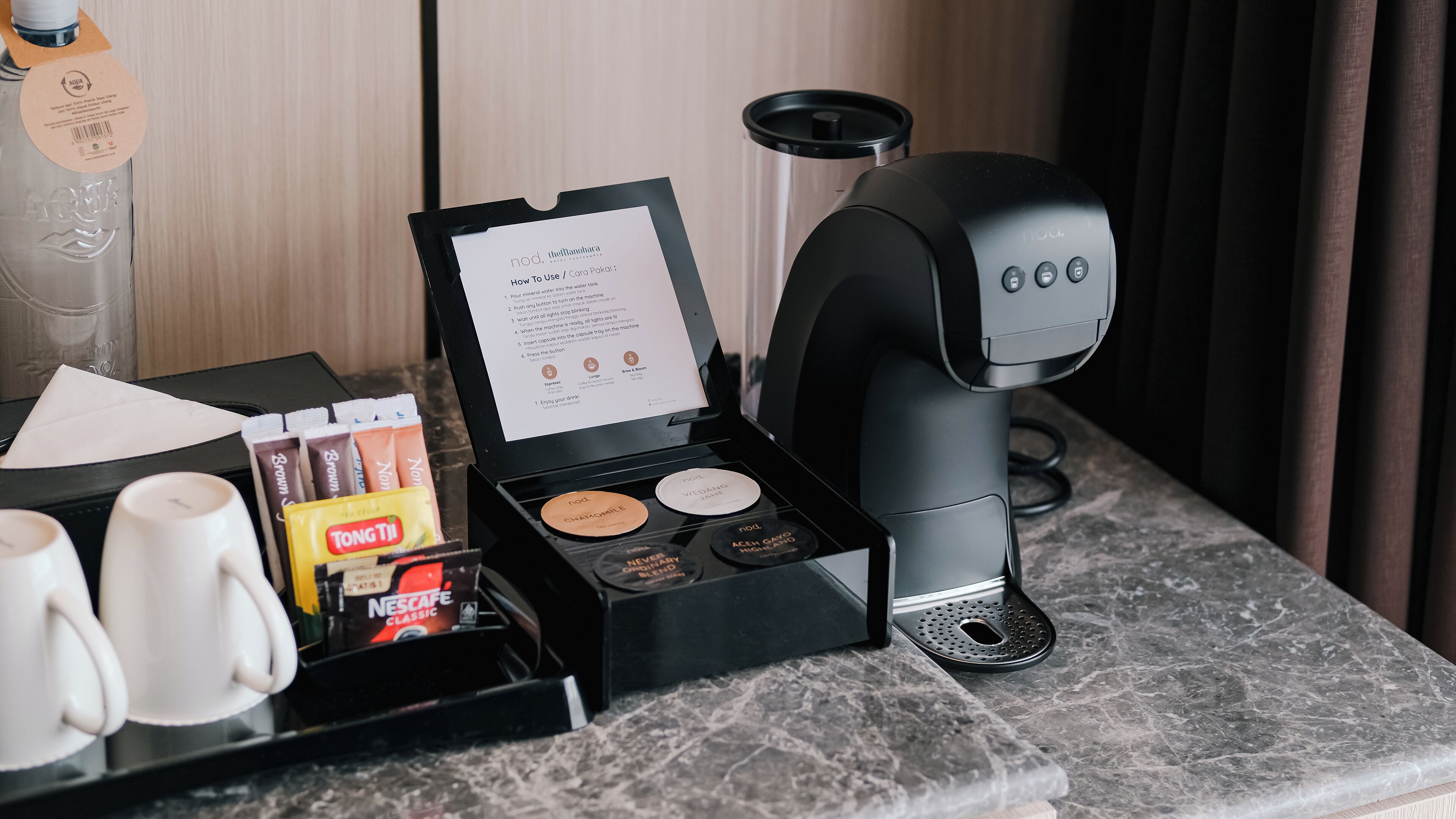 A coffee machine with a manual and a tray of coffee pods and cups on a marble countertop.