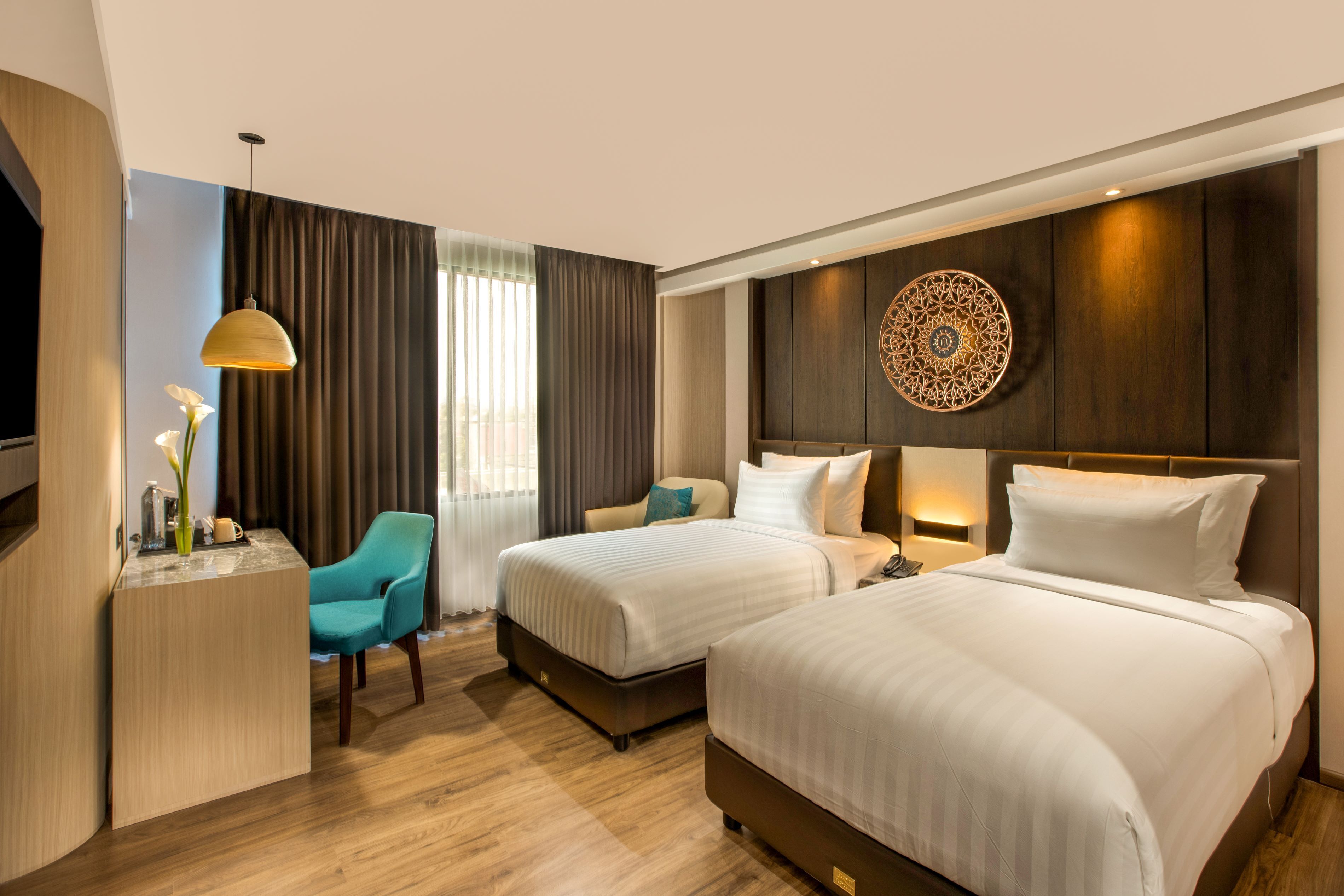 A hotel room with two beds, a desk, a chair, a TV, and a decorative wall piece.