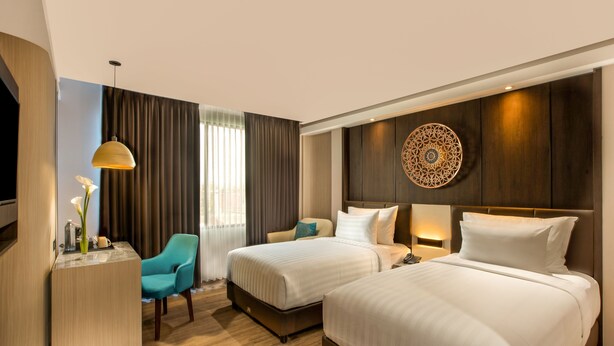 A hotel room with two beds, a desk, a chair, a TV, and a decorative wall piece. - The Manohara Hotel Yogyakarta (Depok)