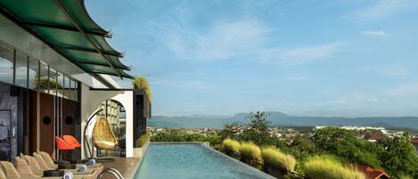 Una piscina infinita en la azotea con sillones de descanso y vistas de la ciudad.