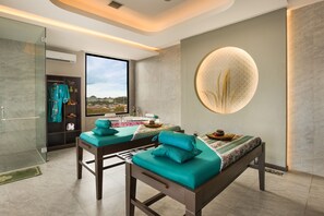A spa room with two massage tables, a large window, and a circular wall feature.
