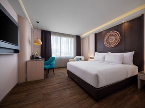 A modern hotel room with a large bed, a desk with a chair, a TV, and a decorative wall piece.