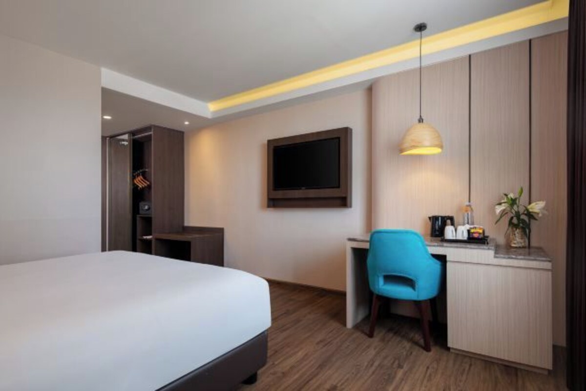 Habitación de hotel con cama, escritorio, silla, televisor y una pequeña kitchenette.