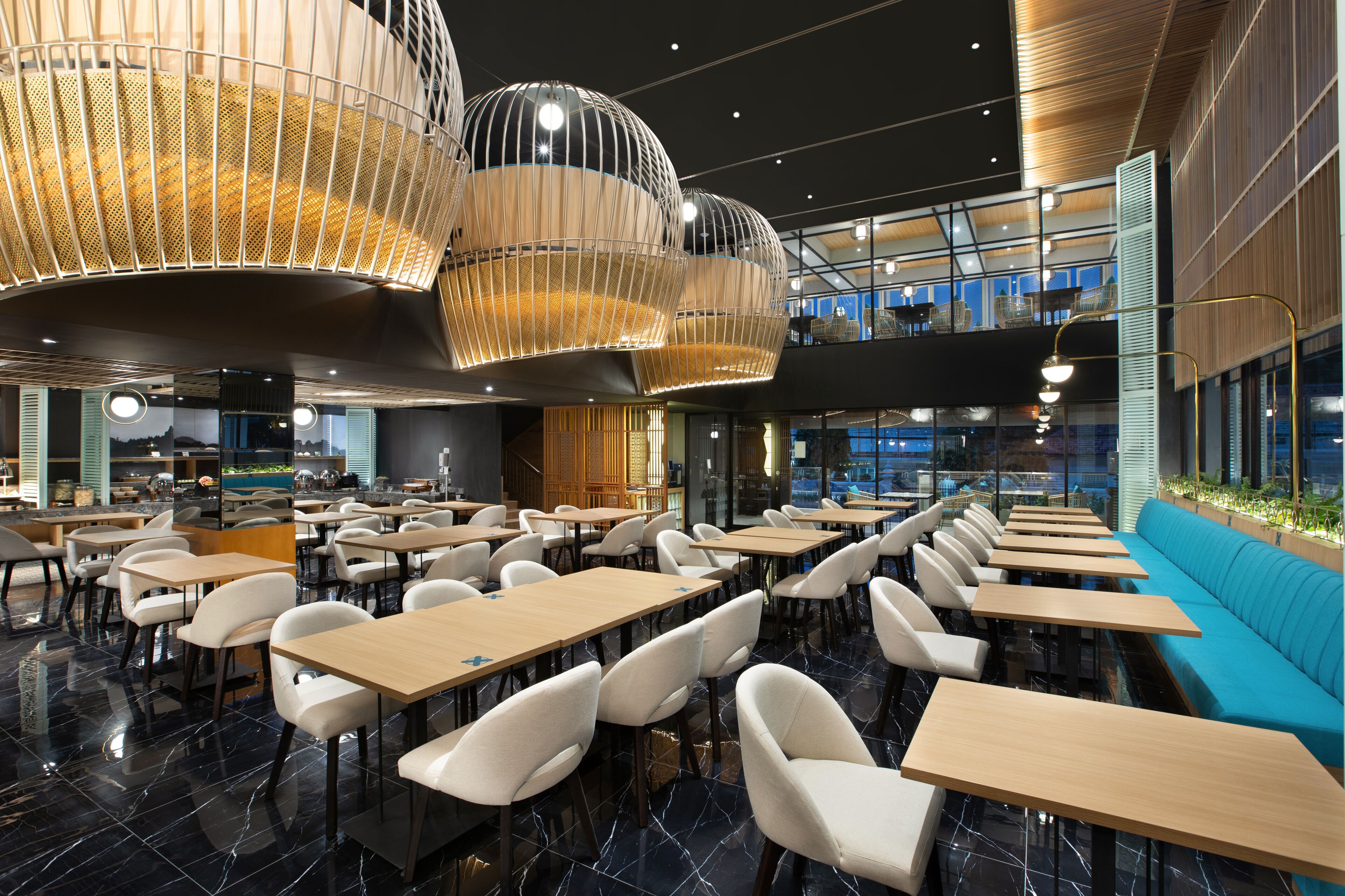 A modern restaurant with multiple dining tables and chairs, a blue seating area, and a unique ceiling design with spherical light fixtures.