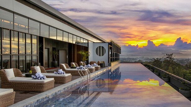 An infinity pool with lounge chairs and a view of the sunset. - The Manohara Hotel Yogyakarta (Depok)