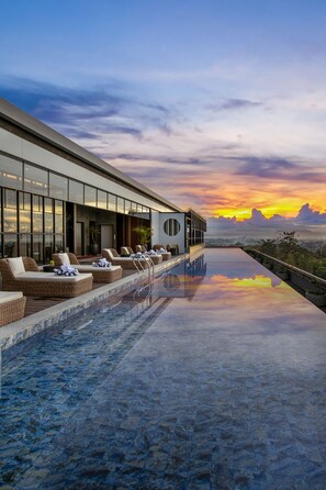 Una piscina infinita con sillones de descanso y vista al atardecer.