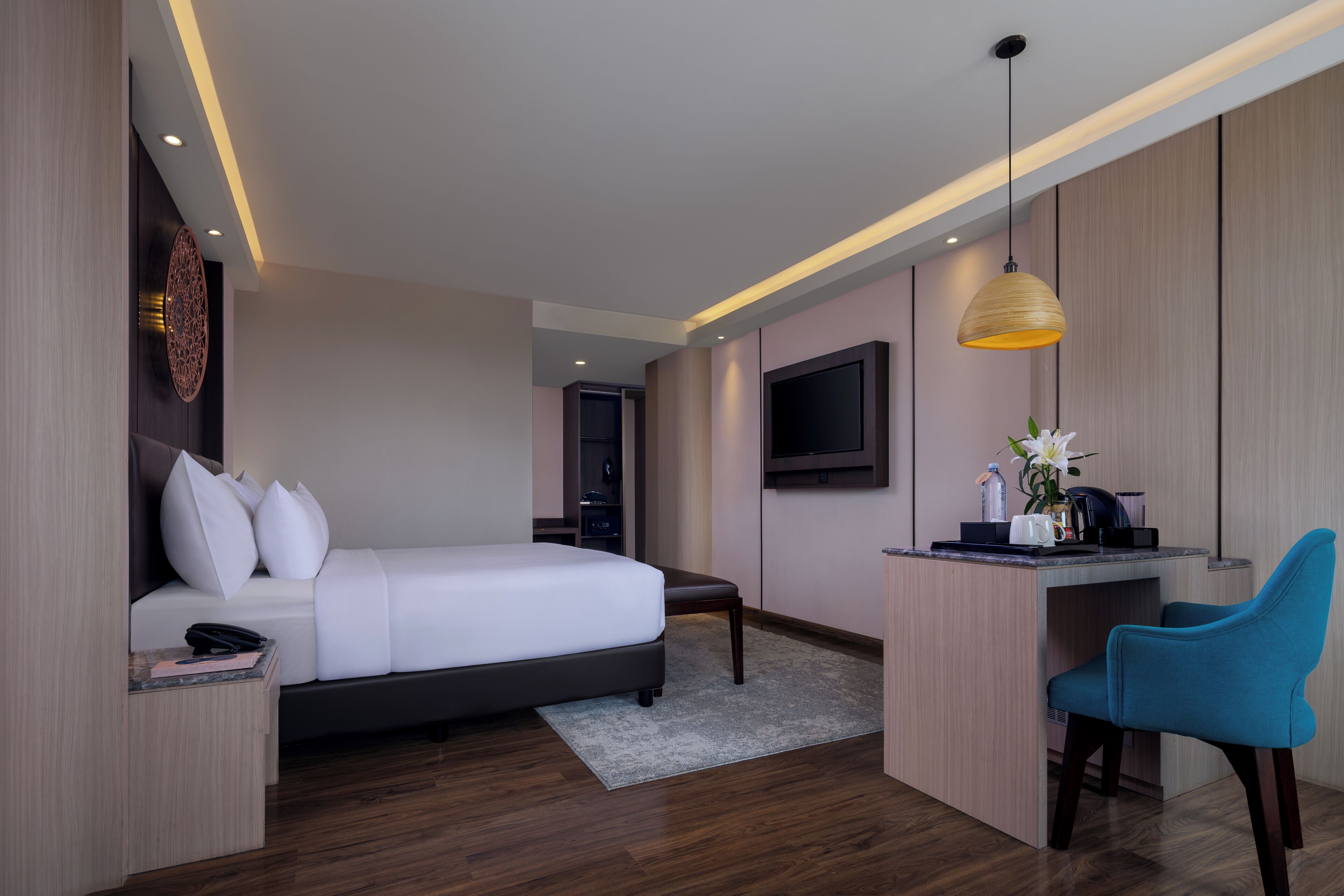 Une chambre d’hôtel moderne équipée d’un lit, d’un bureau, d’une chaise et d’un téléviseur fixé au mur.