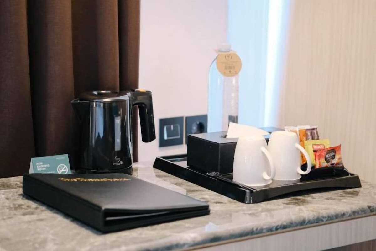 Habitación de hotel con estación de café, que incluye cafetera, tazas y una bandeja con cápsulas de café.