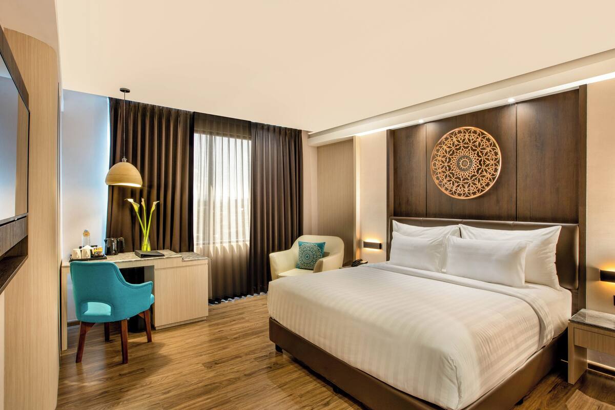 A hotel room with a bed, desk, chair, and a decorative wall piece.