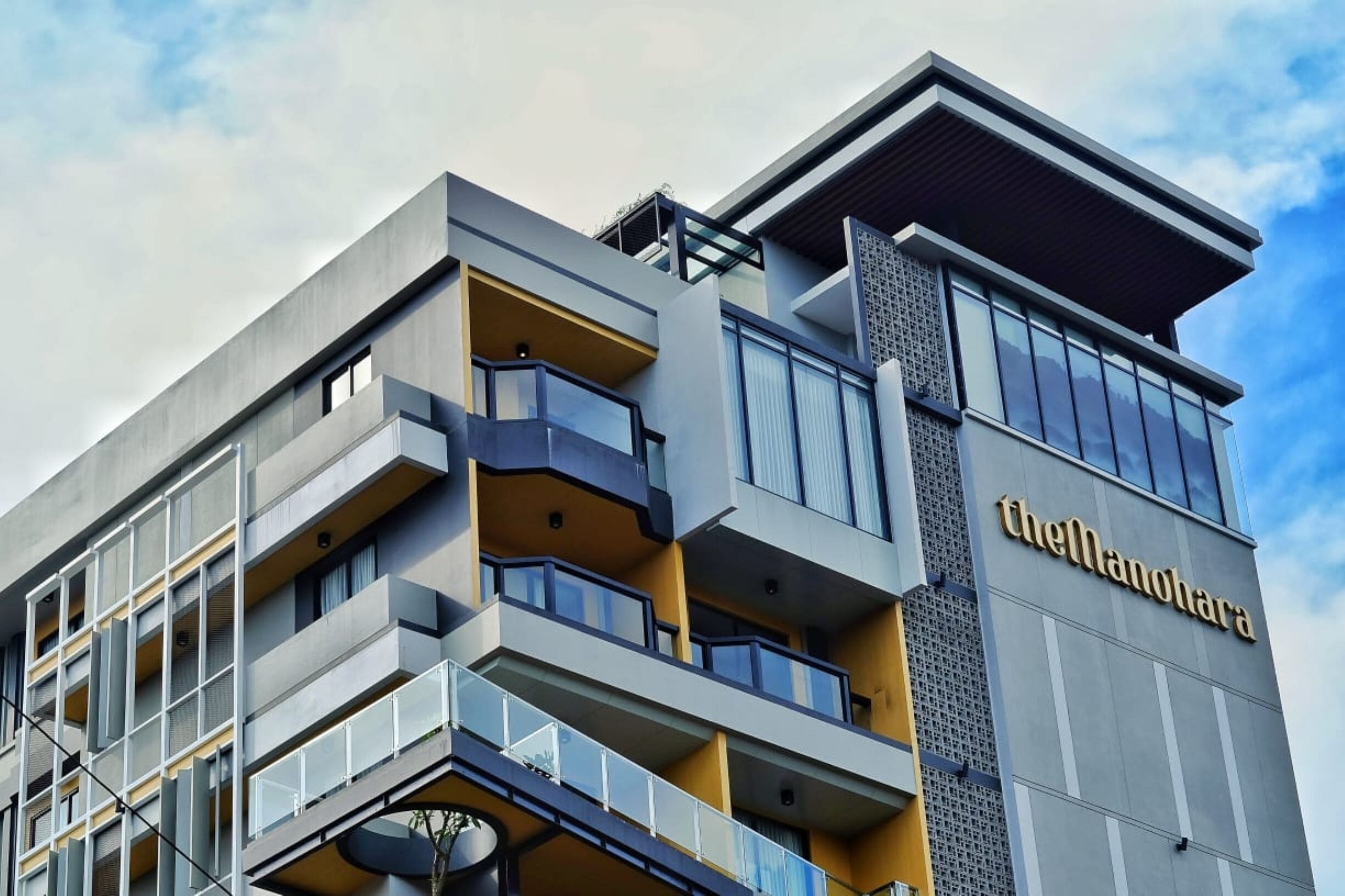 A modern hotel with multiple balconies, a prominent name sign, and a mix of glass and concrete architecture.