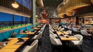 A modern restaurant with a long dining area, high ceilings, and a mural on the wall. - The Manohara Hotel Yogyakarta (Depok)
