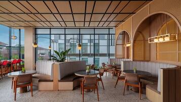 Um restaurante moderno com mesas redondas, assentos acolchoados e grandes janelas que oferecem vista da cidade.