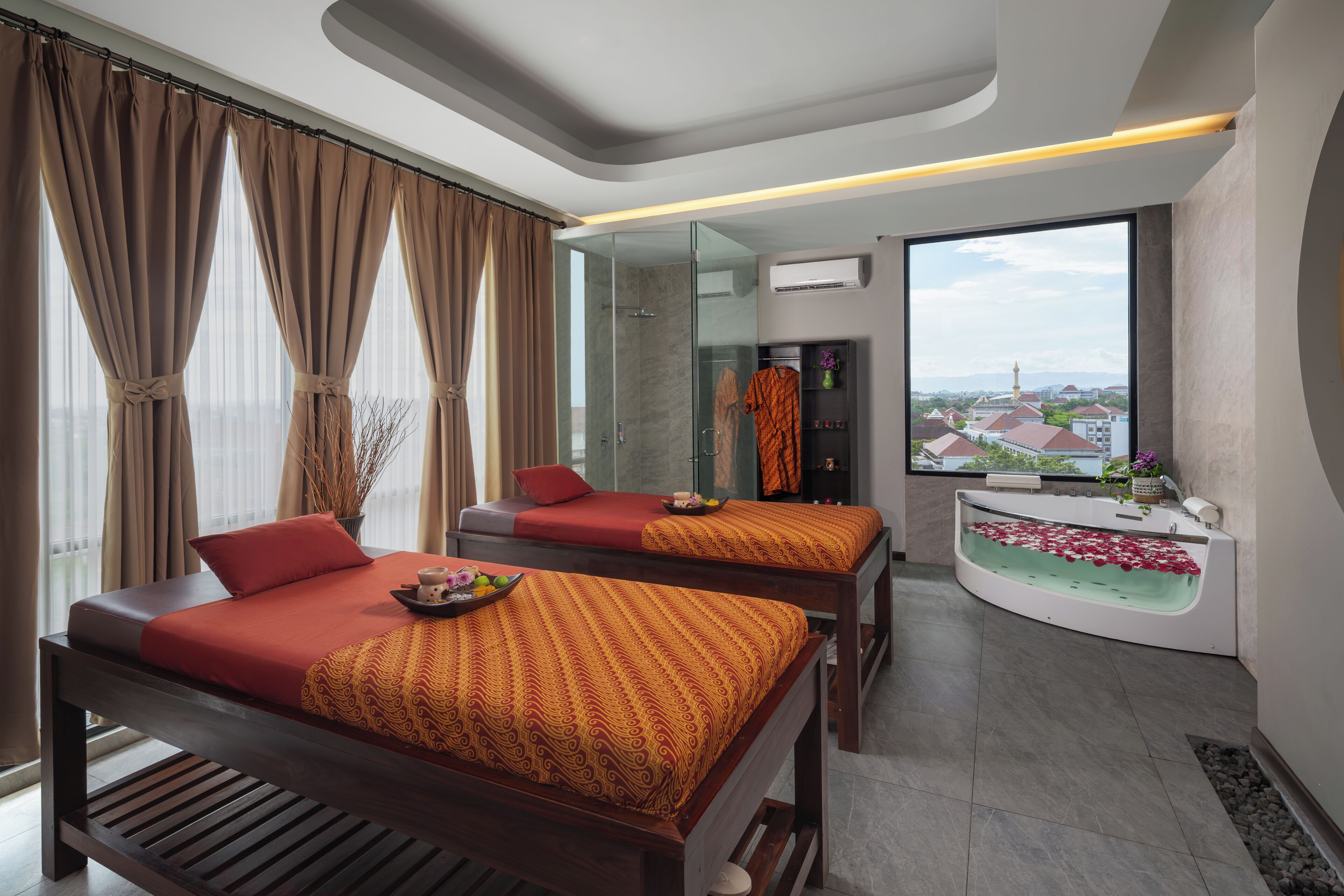 A modern hotel room with two beds, a glass shower enclosure, a bathtub with rose petals, and a city view.