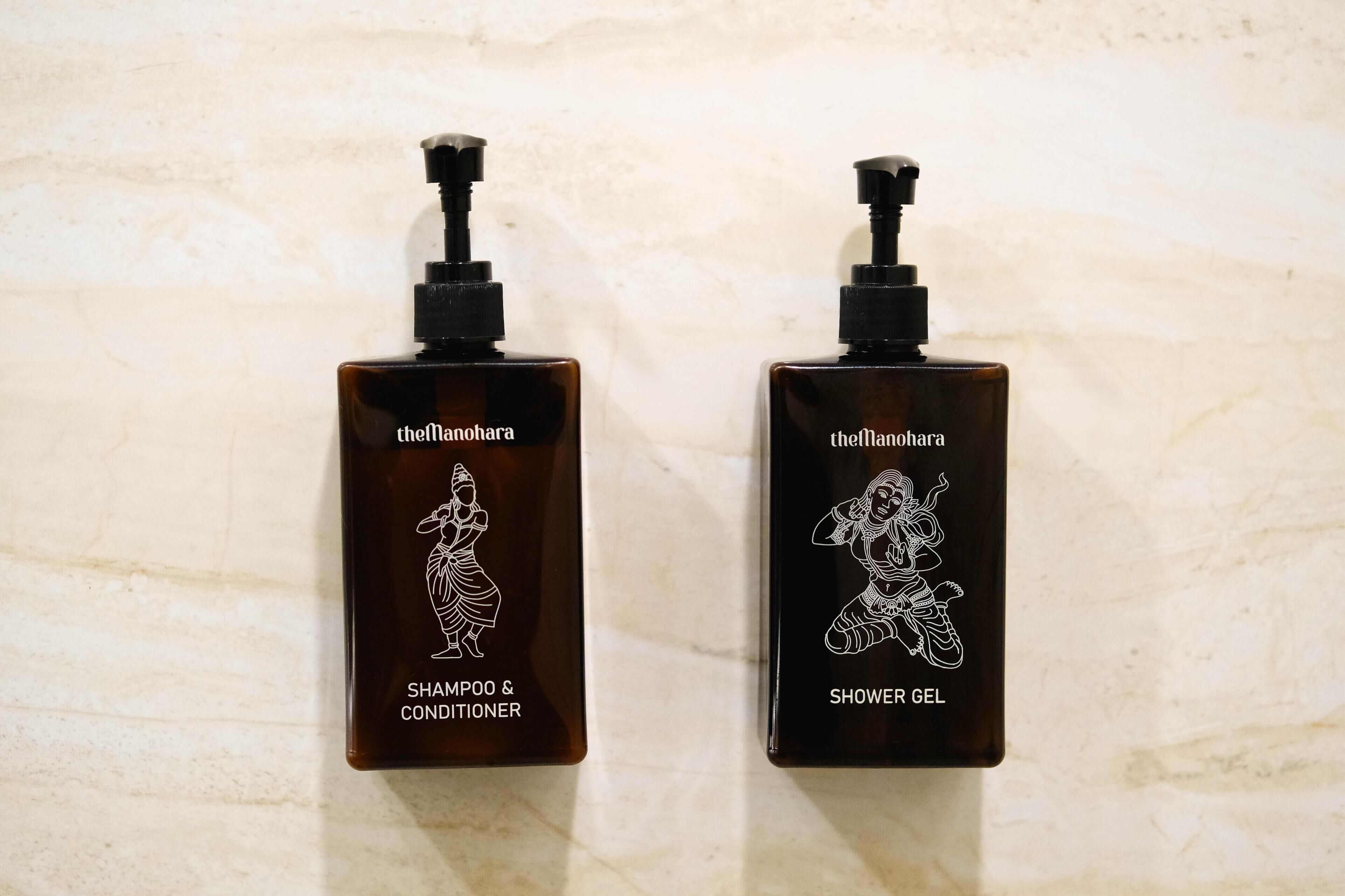 Zwei Flaschen Manohara Shampoo, Conditioner und Duschgel vor einer strukturierten Wand.