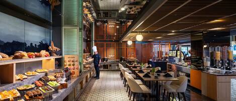 A restaurant with a variety of food items on display, a waiter standing, and a seating area with tables and chairs.