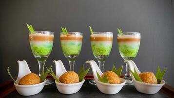 Cuatro vasos de postre en capas con cobertura verde, cada uno con una tetera blanca y un tazón de bolitas redondas y doradas.