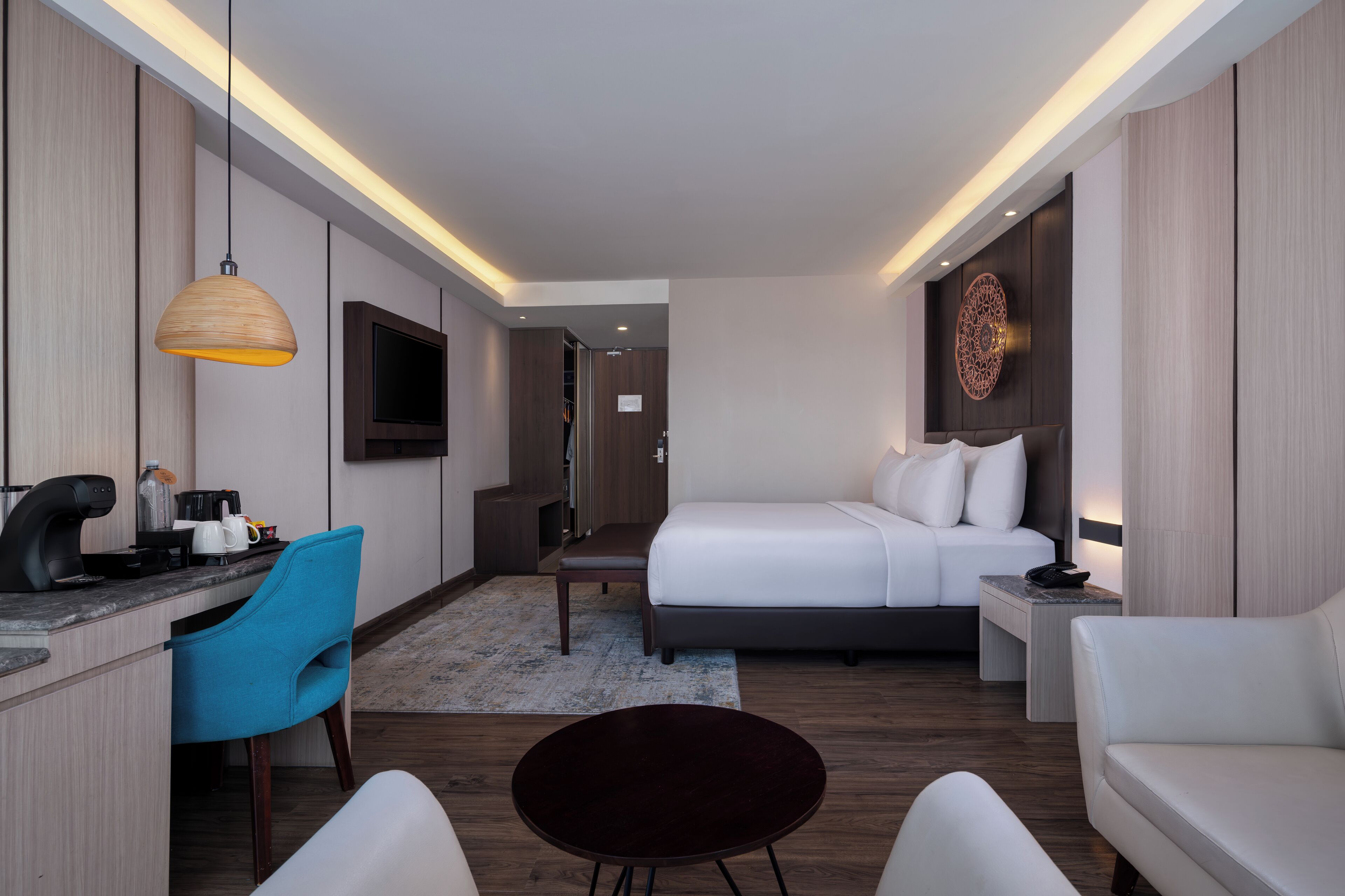 Una habitación de hotel moderna con una cama, un escritorio con silla, un televisor y un adorno en la pared.